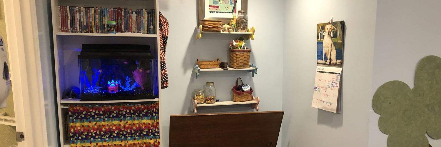 A lit fish tank on a bookshelf of children’s films, beside small wall shelves of baskets and jars