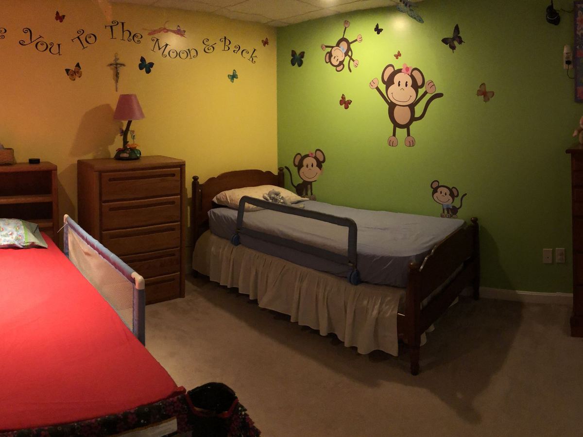 The nap room: two small beds with safety rails, a dresser and lamp, and a green wall painted with cartoon monkeys and butterflies