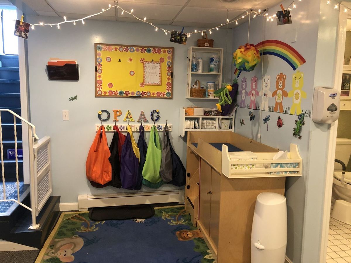 The changing area: a changing table beside a painted rainbow on a pale blue wall, with a row of children’s bags on hooks